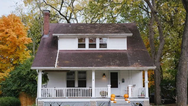 White house with porch and autumn trees.