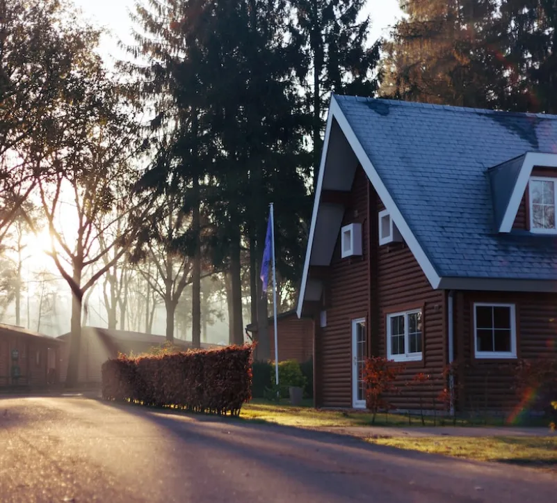 Sunrise over cozy wooden house in misty forest.