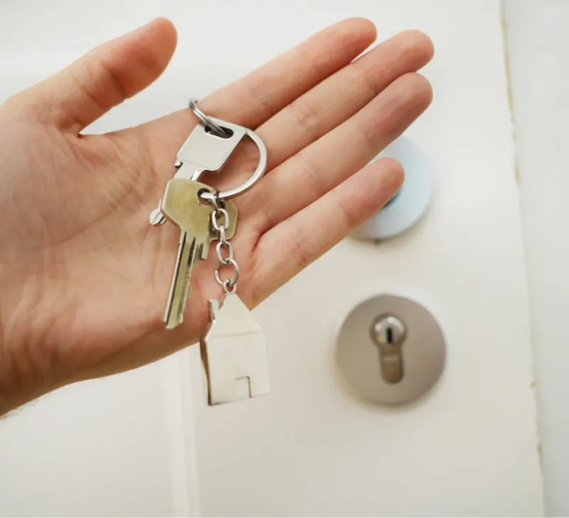 Hand holding house keys near door lock.