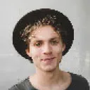 Young man smiling with curly hair wearing a hat.