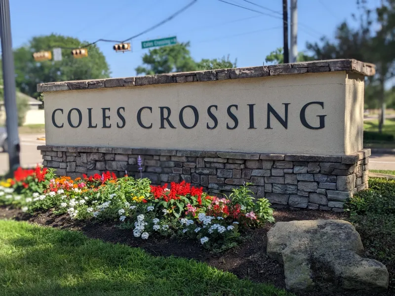 Coles Crossing sign with flowers on sunny day.