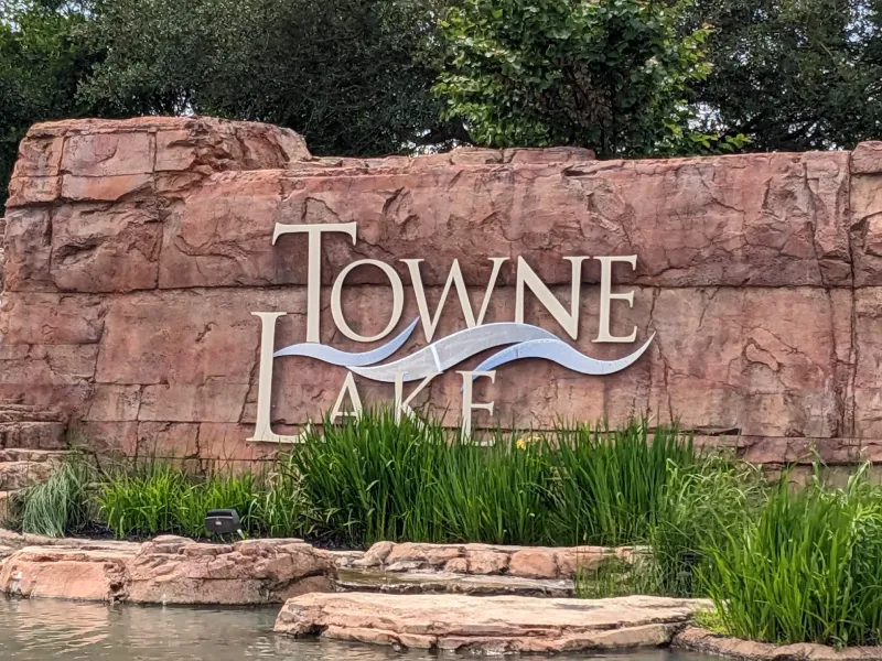 Towne Lake" sign on stone wall with greenery and water